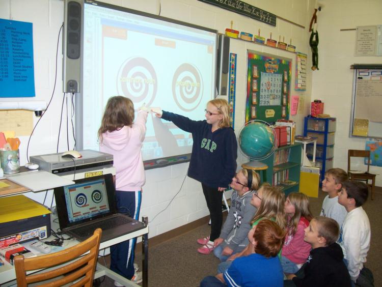 Two students standing at a whiteboard as other sitting students watch